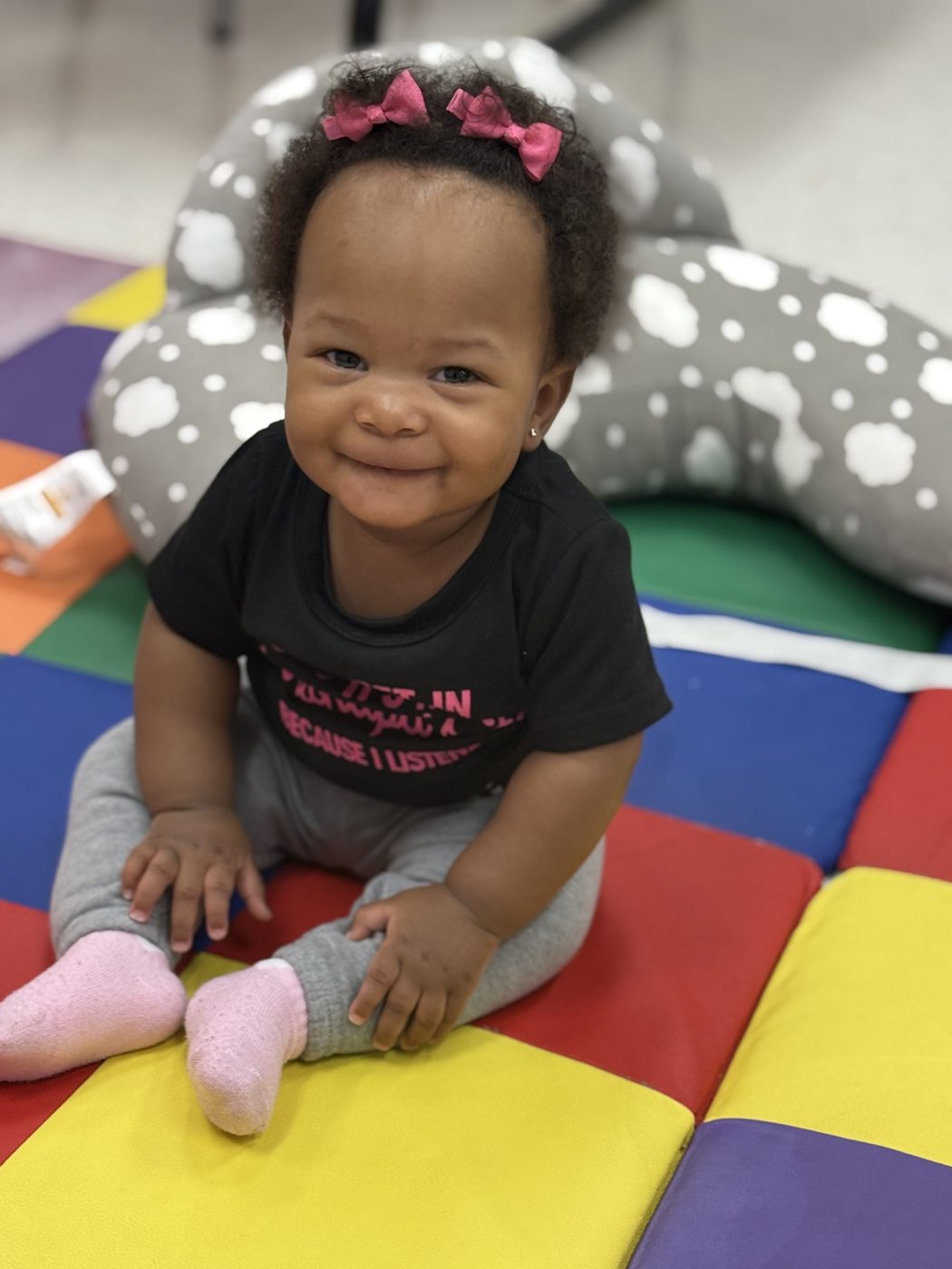 Smiling baby sitting up on a colorful play mat in the Gifted Minds infant room